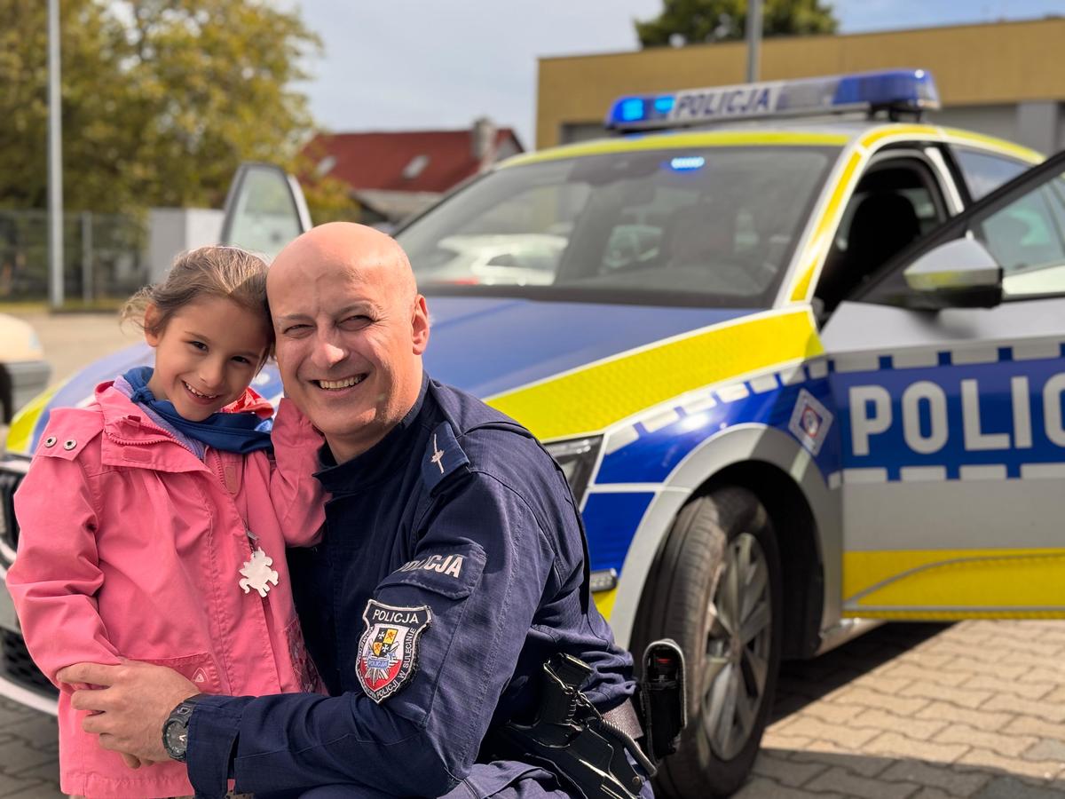 Policjant z córeczką na tle radiowozu. 