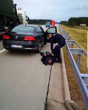 Policjant podczas zatrzymania kierowcy mitsubishi. Mężczyzna leży na jezdni z założonymi kajdankami. Obok nieoznakowany radiowóz.