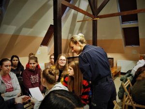 Policjantka pochyla się nad grupą uczniów wykonujących pracę w zespole, w ramach prowadzonych zajęć.