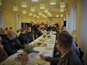 Policjanci i zaproszeni goście siedzą przy wigilijnym stole. Wszyscy ubrani są w mundury galowe.