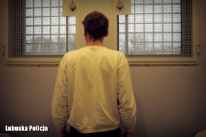 Zatrzymany mężczyzna stoi tyłem do zdjęcia wewnątrz policyjnej celi.