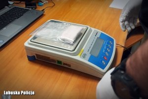 Waga elektroniczna. Na niej znajduje się woreczek strunowy z białym proszkiem.