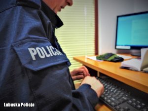 Policjant siedzi przy biurku, korzysta z komputera. Sporządza dokumentację służbową.