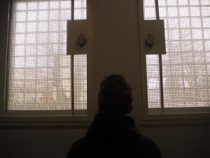 Zatrzymany mężczyzna stoi tyłem do zdjęcia na tle okien policyjnej celi.