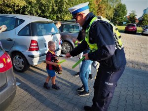 Policjant ruchu drogowego wręcza uczniom odblaskowe elementy.