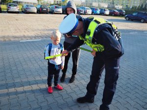 Policjant ruchu drogowego wręcza chłopcu odblaskową opaskę.