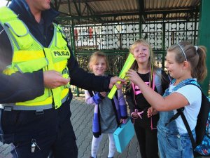 Policjant ruchu drogowego wręcza uczennicą odblaskowe opaski.