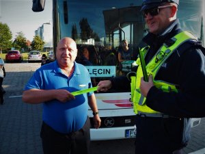 Policjant wręcza odblask kierowcy szkolnego autobusu.