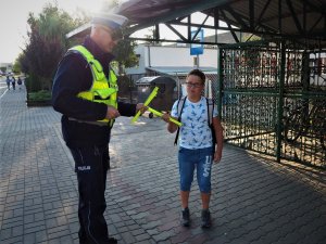 Policjant wręcza odblaskową opaskę uczniowi.