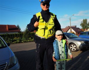 Policjant pozuje do wspólnego zdjęcia z przedszkolakiem trzymającym odblask.