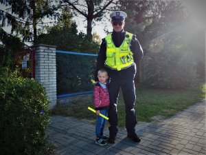 Policjant pozuje do wspólnego zdjęcia z przedszkolakiem trzymającym odblask.