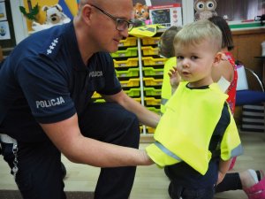 Policjant zakłada chłopcu kamizelkę odblaskową.