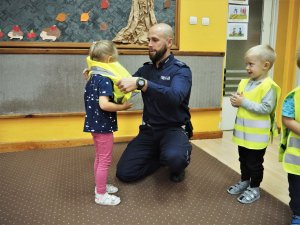 Policjant zakłada dziewczynce kamizelkę odblaskową.