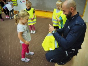 Policjant ubiera dziewczynce kamizelkę odblaskową.