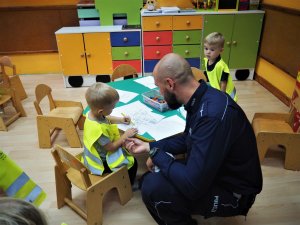 Policjant z chłopcem w kamizelce odblaskowej przy stoliku.