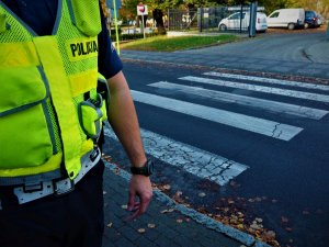 Odblaskowa kamizelka policjanta na tle przejścia dla pieszych.