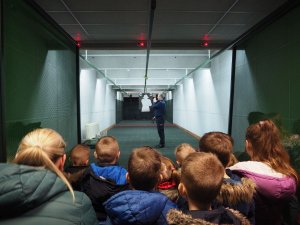 Policjant na strzelnicy wyjaśnia dzieciom jak wygląda strzelanie do tarczy.