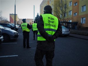 Policjant z żołnierzami Wojsk Obrony Terytorialnej podczas sprawdzenia wzrokowego i telefonicznego osoby przebywającej na kwarantannie.