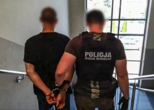 Policjant prowadzi zatrzymanego mężczyznę.