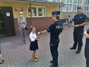 Policjantka wręcza odblaskową zawieszkę dziewczynce.