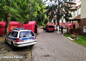 Przed budynkiem szpitala stoi pojazd medyków, dalej namiot i samochód straży pożarnej.