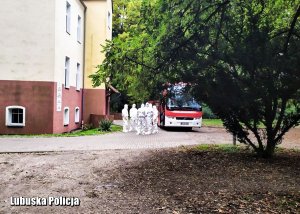 Przed budynkiem szpitala przy autobusie stoją medycy ubrani w kombinezony ochronne.