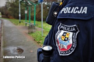 Na pierwszym tle widoczne jest rękaw policyjnego munduru z logiem logiem Komendy Powiatowej Policji w Sulęcinie. Na drugim planie widoczna jest wiata przystanku autobusowego.