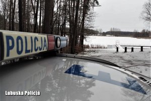 Belka radiowozu, w tle ośnieżony las i jezioro.