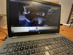 Na na biurku stoi laptop. Na jego ekranie, widoczny jest policjant i policjantka. Oboje mają na twarzach maseczki.