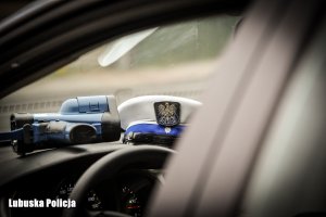 Na kokpicie radiowozu znajduje się laserowy miernik prędkości, obok leży czapka policjanta ruchu drogowego.