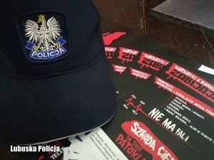 Granatowa czapka z daszkiem. Na niej orzeł i napis Policja. Obok broszury na temat dopalaczy i narkotyków z napisem Szkoda Ciebie na takie patoklimaty.