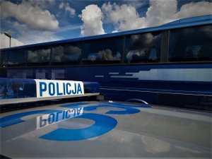 Belka radiowozu z napisem Policja. W tle autobus.