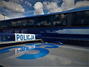 Belka radiowozu z napisem Policja. W tle autobus.