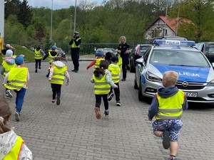 Dzieci biegną stronę policjanta ruchu drogowego. który mierzy ich prędkość ręcznym miernikiem prędkości.