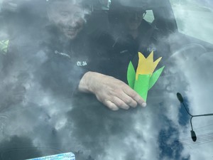 Policjant ruchu drogowego kładzie na kokpicie auta kwiatka wykonanego przez przedszkolaki.