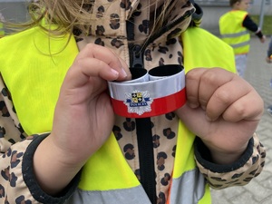 Dziewczynka trzyma w dłoniach odblaskową zawieszkę z flagą Polski i logo sulęcińskiej jednostki.