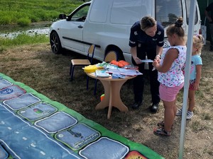 Policjanta stoi z dwiema dziewczynkami przy stoliku, podczas gdy wybierają one nagrody za udział w grze.