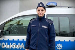 Posterunkowa Patrycja ma na sobie policyjny mundur. Stoi na tle oznakowanego radiowozu.