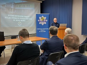 Komendant Powiatowy Policji w Sulęcinie stoi przy mównicy. Przedstawia wyniki pracy policjantów w 2022 roku. W tle ekran z wyświetloną prezentacją.