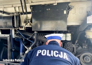 Policjant zagląda pod pokrywę silnika autobusu.