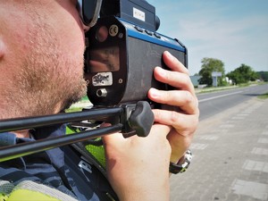 Policjant wykonuje pomiar prędkości laserowym miernikiem prędkości.