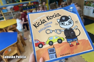 Książeczka &quot;Kicia Kocia zostaje policjantką&quot; w tle bawiące się dzieci.