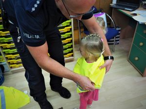 Policjant ubiera dziewczynce kamizelkę odblaskową.