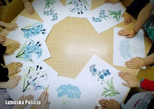 Dzieci trzymają rączki na swoich rysunkach, które leżą na stole.