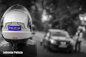 Kask ochronny z napisem Policja. W tle policjant kontrolujący pojazd osobowy.