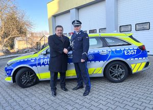 Wójt Gminy Słońsk i Komendant Powiatowy Policji w Sulęcinie podają sobie dłonie na tle oznakowanego radiowozu.