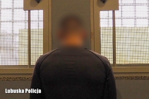 Zatrzymany mężczyzna stoi tyłem do zdjęcia w celi, na tle okratowanych okien.