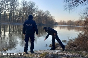 Policjanci stoją nad brzegiem rzeki, wokół zimowa aura.