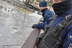 Policjanci stoją na pomoście, zaglądają w stronę zamarzniętego jeziora.