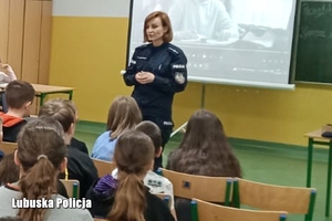 Policjantka prowadzi spotkanie edukacyjne dla uczniów klas IV oraz V. Dzieci siedzą na krzesłach, tyłem do zdjęcia.